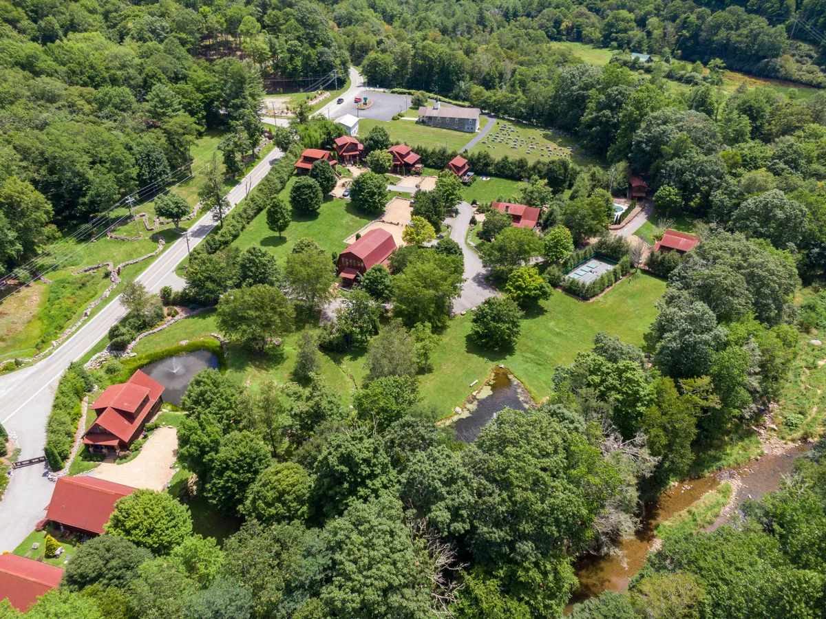 A wide shot of red-roofed cabins nestled among lush green lawns, with meandering walking paths and serene ponds. The scene feels lively yet peaceful, ideal for family gatherings and outdoor play. The landscape is open and inviting, suggesting ample room for family activities and exploration.