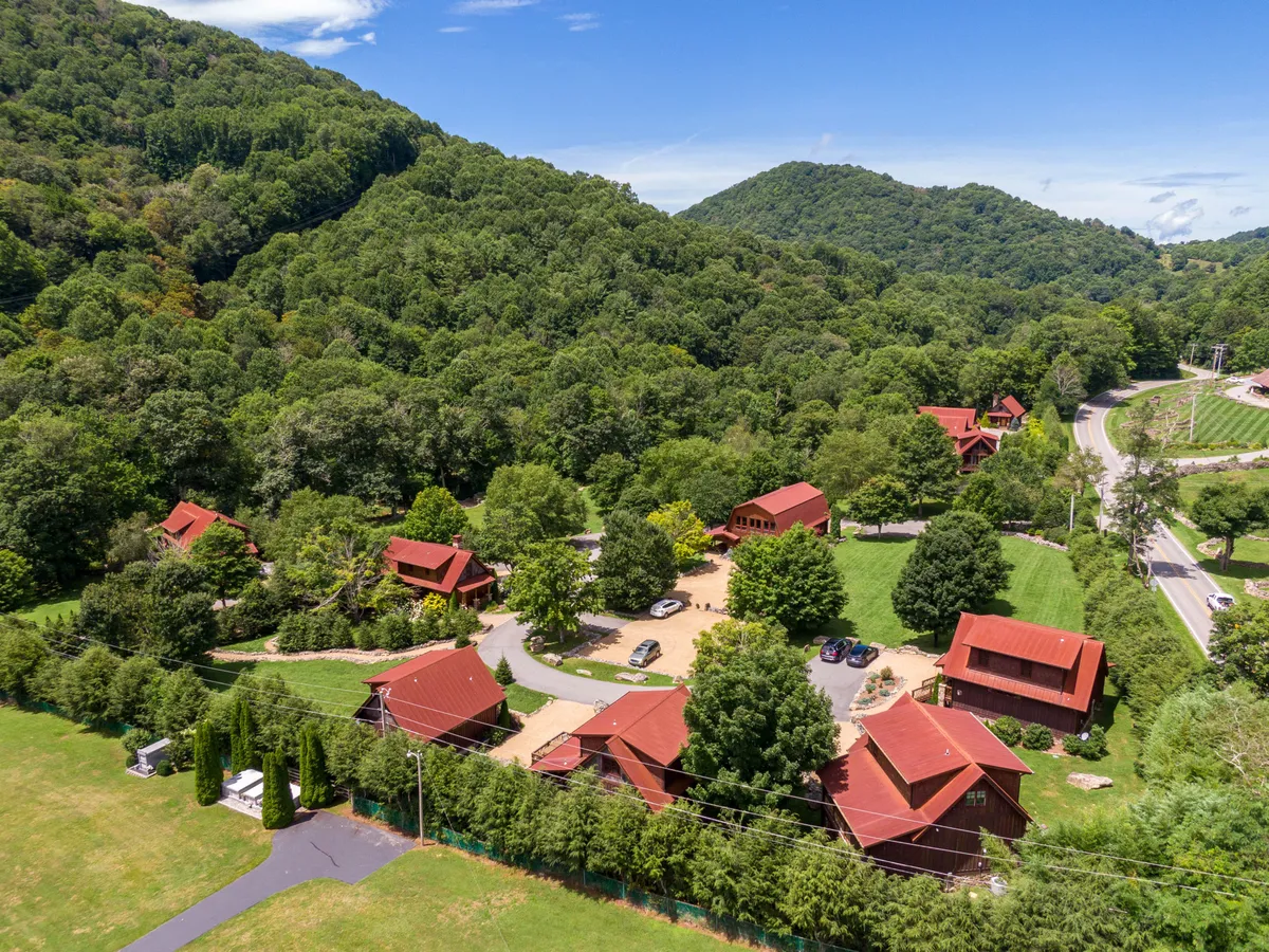 A cluster of rustic cabins surrounded by lush greenery and set against a mountain backdrop. A winding road weaves through the landscape, conveying a sense of seclusion and an invitation to explore. The setting is peaceful and ideal for nature walks or sipping morning coffee outside.