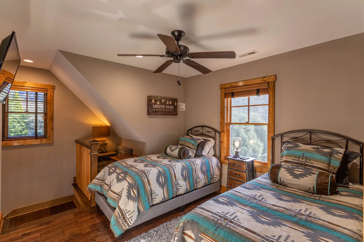 A welcoming loft space with two twin beds adorned in patterned bedding, wooden accents, and a window offering a scenic view. The area feels both playful and cozy, perfect for children or friends.