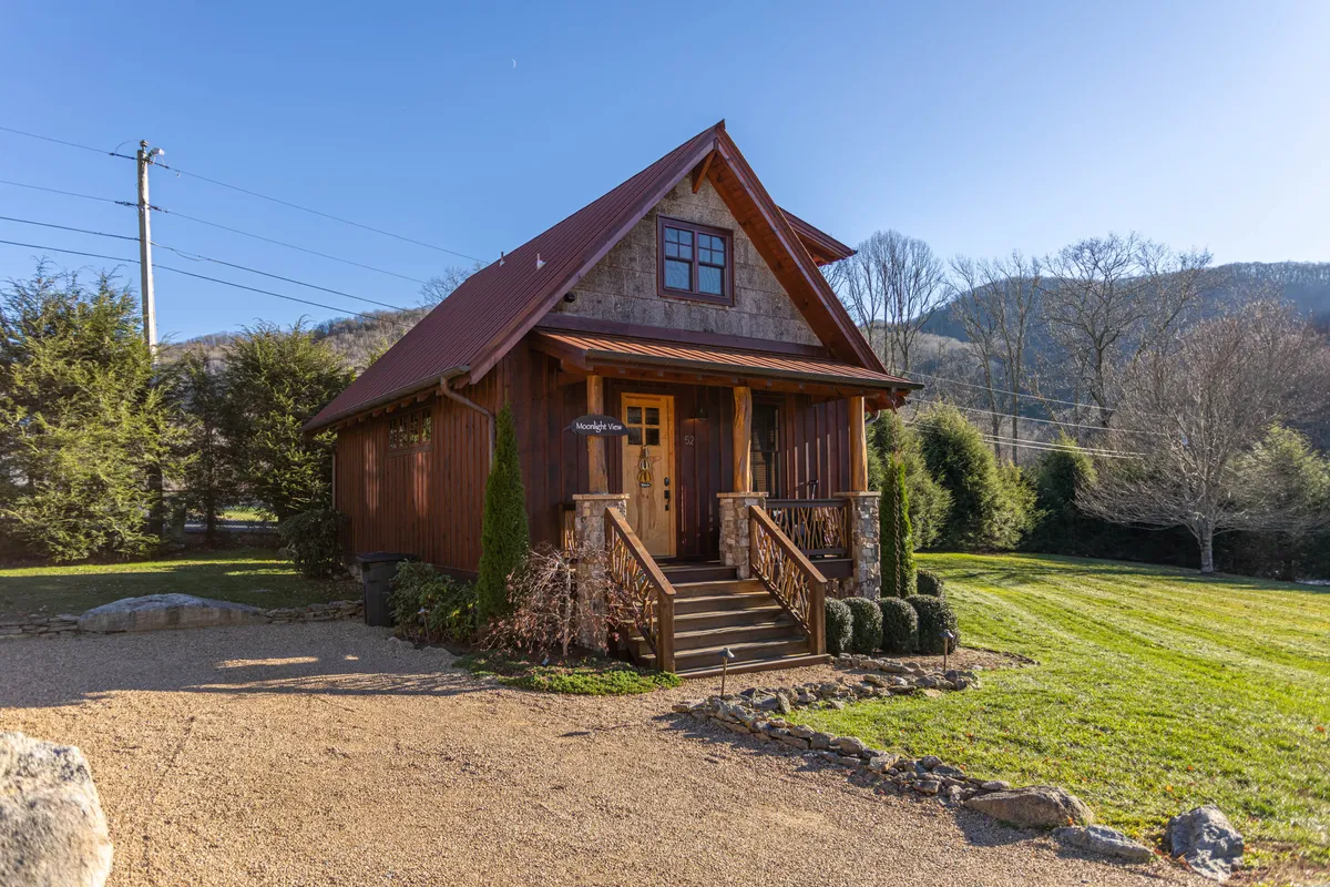 An exterior shot featuring a welcoming porch with wooden steps, a sloped roof, and a lush green lawn. The image suggests relaxation after an adventure, with the porch overlooking an expanse of nature ideal for exploring nearby trails.