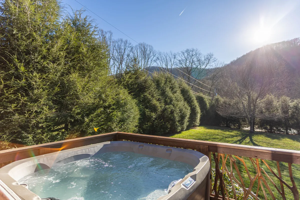 A tranquil scene featuring a hot tub nestled among trees with a stunning mountain view backdrop. The setting is perfect for unwinding, socializing, and soaking in natural beauty, conveying privacy and immersion in nature.