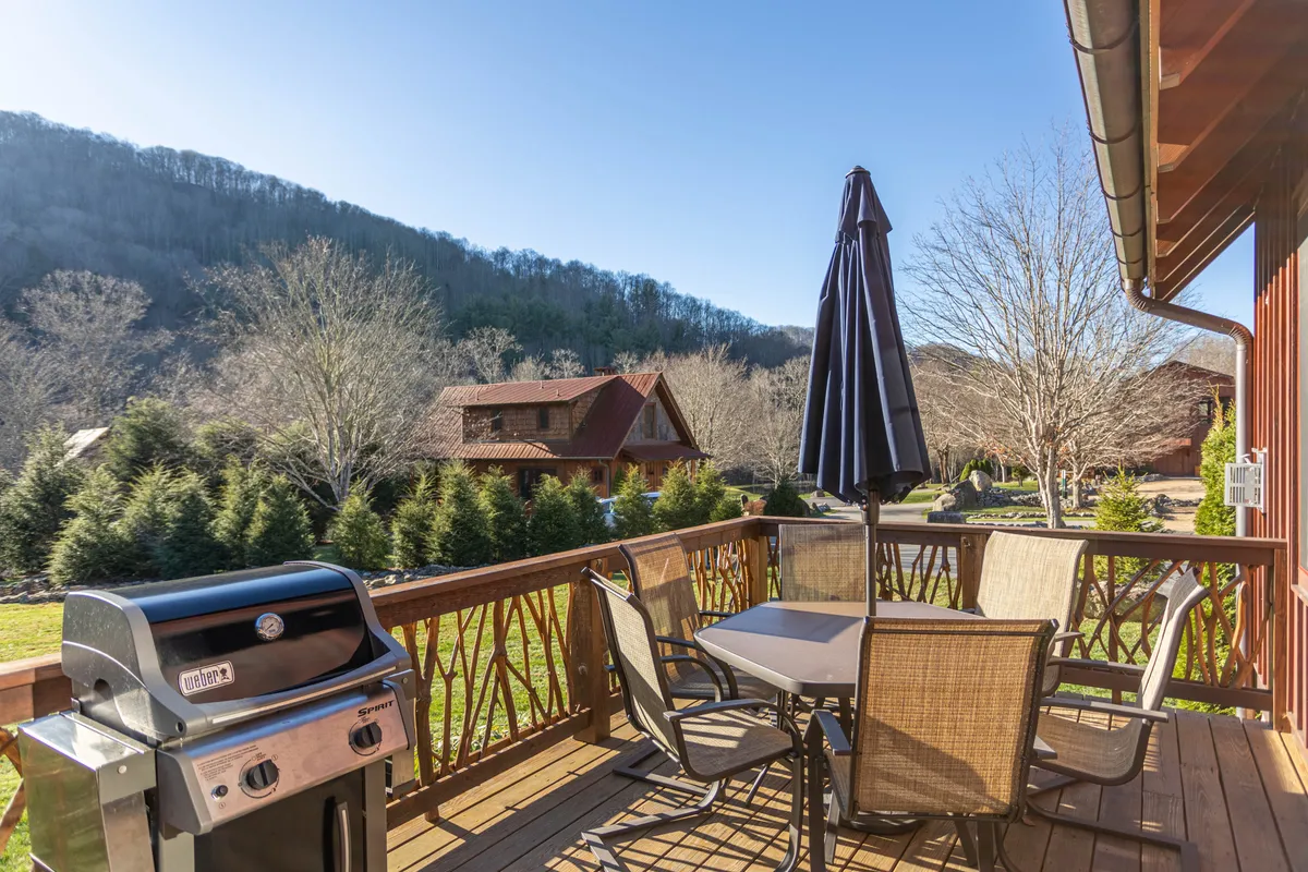 An exterior deck featuring a barbecue grill, outdoor dining set with umbrella, and expansive mountain views. The space is set up for al fresco meals, relaxation, and soaking in the natural beauty that surrounds Eagles Nest.