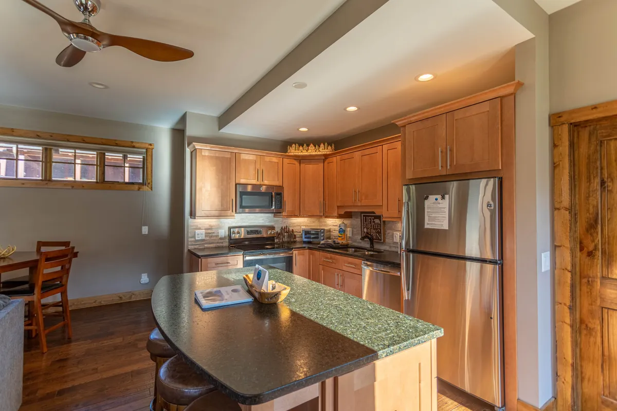 A warm, open kitchen and dining area with a central island, wood cabinetry, stainless steel appliances, and a dining area just beyond. The layout encourages interaction during meal prep, family breakfasts, or festive toasts, capturing the seamless flow between kitchen and dining spaces.