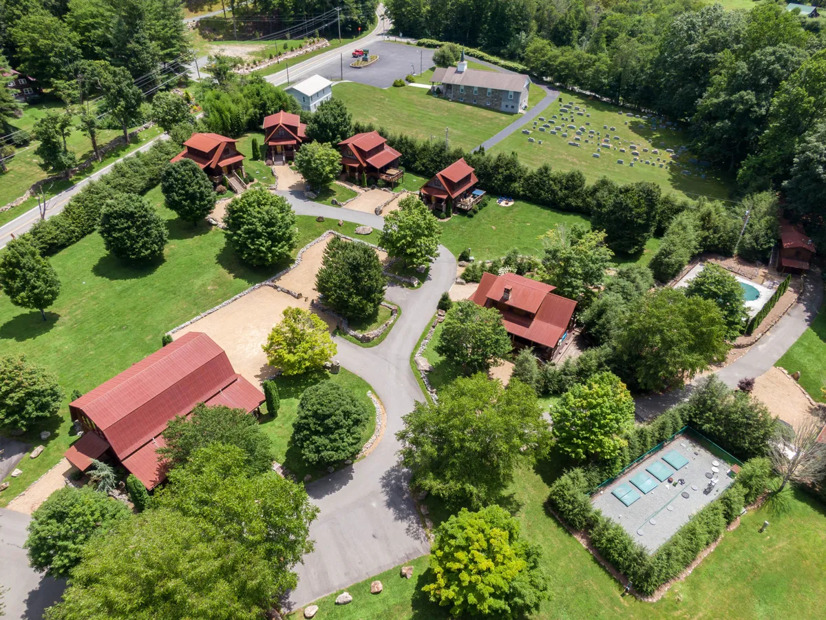 This exterior image depicts rustic cabins surrounded by manicured lawns, a swimming pool, and interconnected pathways. The scene is lively and communal, suggesting plenty of room for group gatherings and outdoor activities within a resort-like setting. The natural landscaping and open spaces imply both adventure and comfort.